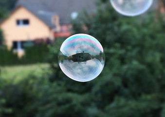 A one big bubble flying in the air. Bubble serve as mirror so we can see some house and cloudy. Bubble is mainly created from green and purple colour