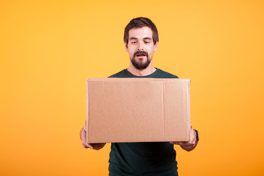Portrait of handsome young man holding a box in his hands. Delivery man on yellow background
