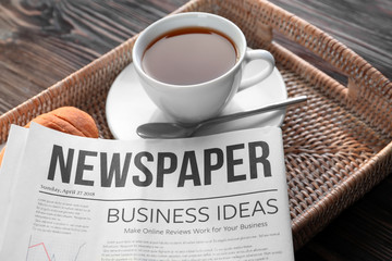 Tray with newspaper and cup of tea on wooden background