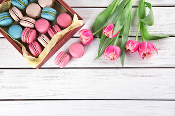 Crate with tasty macarons and tulips on wooden background, top view