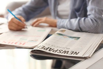 Young woman looking for job in newspapers indoors