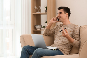 Young freelancer talking on phone while using laptop at home