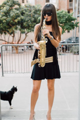 Young brunette girl having fun playing sax outdoor in a urban scene