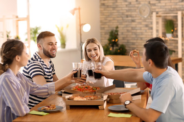 Young people clinking glasses at table indoors