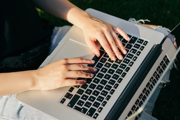 Close-up image of female hands working on laptop, while sitting on grass in the park. Outdoors.