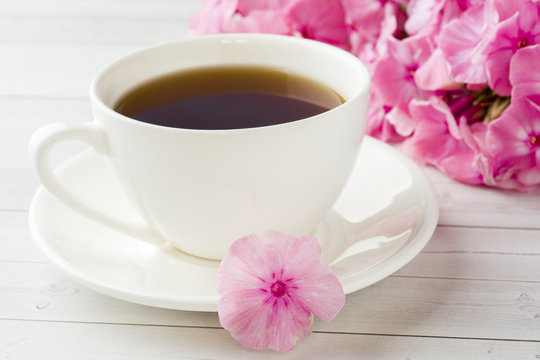 Fototapeta Cup of coffee on a white table and flowers of pink Phlox. The concept of morning Breakfast.