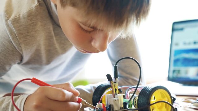 The boy constructs an electronic robot model. Measures the signal in the electrical circuit. Very passionate about his work. 4K video with shallow depth of field focus on hands.