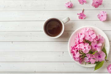 Fototapeta na wymiar Pink Phlox flowers and a Cup of coffee on a white table. Free space for text