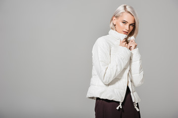 stylish woman in white jacket looking at camera isolated on grey background