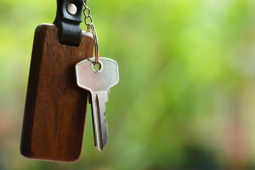 House keys with wooden home keyring with green garden background, property concept, copy space
