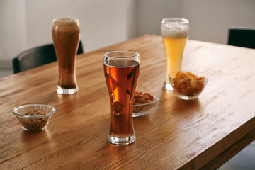 Glasses with different sorts of beer and snacks on table in bar