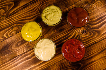 Different sauces in glass bowls on wooden table. Top view