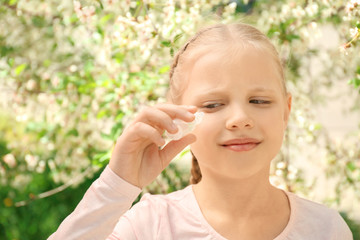 Little girl using eye drops near blooming tree. Allergy concept