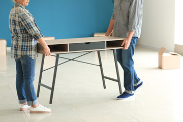 Mature couple carrying table in room after moving to new home