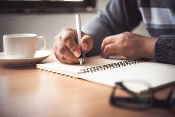 The hand of a man holding a pen and taking notes in a notebook.
