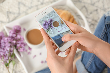 Woman taking photo of blossoming lilac and cup with coffee, closeup