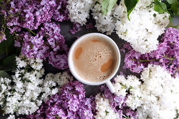 Beautiful blossoming lilac with cup of coffee on table, top view