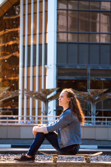 Fototapeta premium a young beautiful girl sitting on a skateboard on the background of a skyscraper