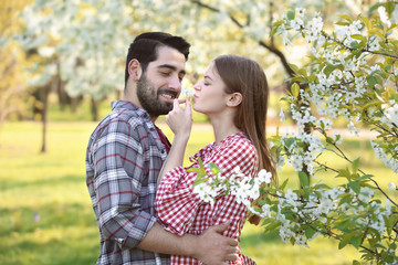 Happy young couple near blooming tree in park on spring day