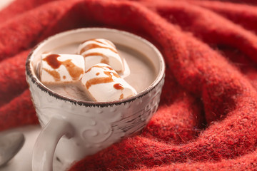 Cup of delicious hot cocoa with marshmallows and fabric on table, closeup