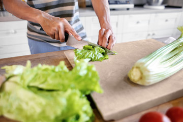 Young African-American man cutting salad in kitchen