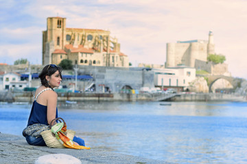 Pretty woman sitting on the edge of the sea in a Spanish port of Castro Urdiales, with a look lost in infinity and the city behind.