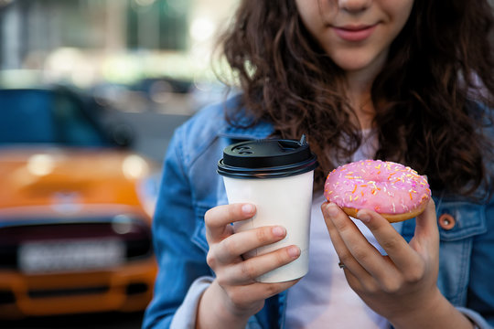 hands holding a donut and coffee on the background of a busy metropolis.