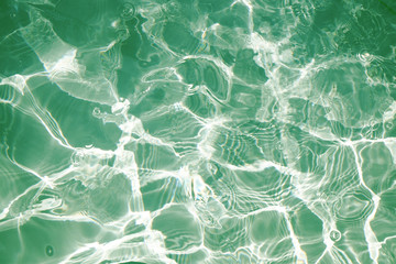 Green water surface with bright sun light reflections, water in swimming pool background closeup