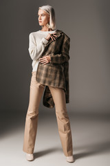stylish elegant model posing in autumn sweater, beige pants and tweed jacket, on grey