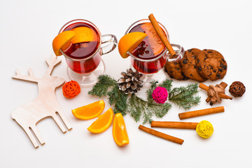 Glasses with mulled wine or hot drink near wooden deer decoration on white background, close up. Mulled wine or hot beverage with cinnamon sticks, orange fruit and fir cone. Winter beverage concept