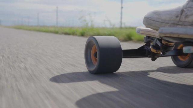 Close up of a longboard wheel riding on asphalt road.