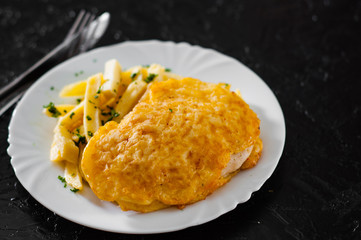 Fish and Chips. Fried fish fillet in cheese and potatoes in a white plate on black background.