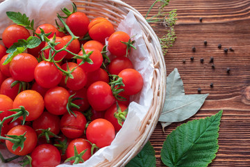 Small red cherry tomatoes spill out of a wicker basket on an old wooden table in rustic style, selective focus