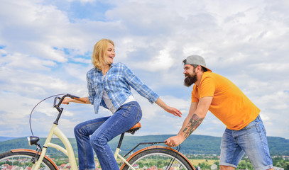 Man pushes girl ride bike. Girl cycling while man support her. Support helps believe in yourself. Feel impulse to start moving. Woman rides bicycle sky background. Push and promoting. Impulse to move