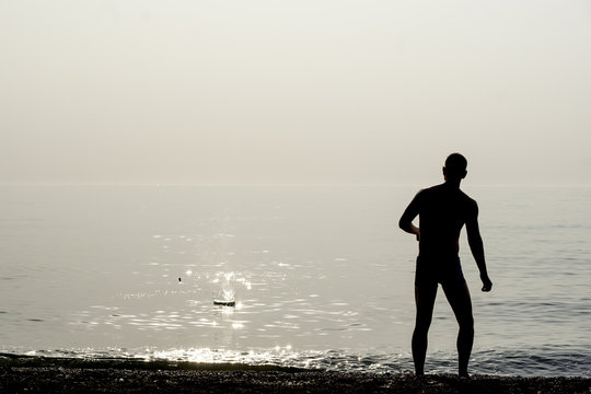 A young man throws stones into the water. Silhouettes.