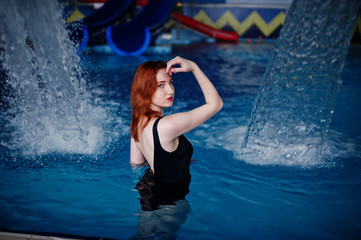 Obraz premium Sexy red haired girl in black swimsuit having rest in swimming pool of aqua park.