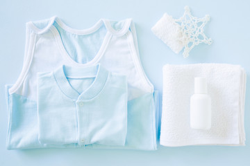 Light blue bodysuit on the pastel blue table in bathroom. White bottle of natural herbal shampoo on towel. Care about kids clean and soft hands, face, legs and body skin. Baby clothes. Soft colors. 