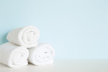 Fresh, fluffy, white towel rolls on shelf in bathroom. Empty place for text on pastel blue wall. Spa still life.