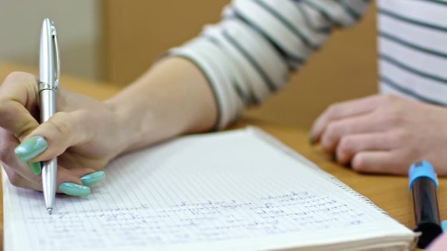 Close up hands of unrecognizable young woman using pen when writing in notebook during lecture at university