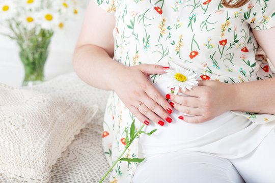 Closeup of pregnant woman holding flower and touching her belly