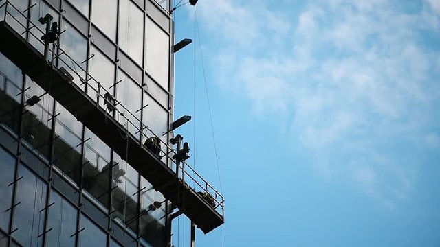 Construction workers on a suspended platform on a skyscraper glass facade