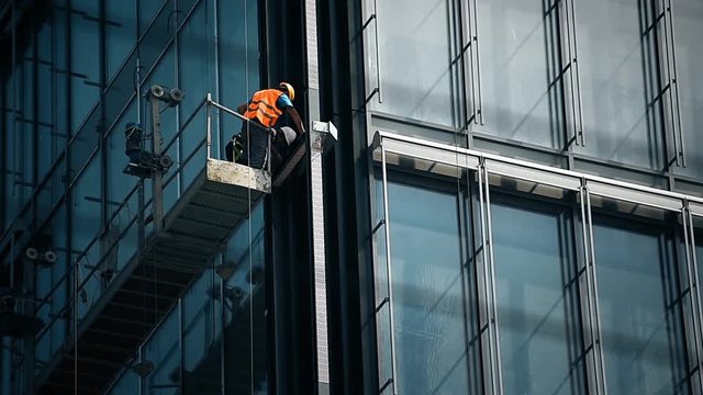 Construction workers on a suspended platform on a skyscraper glass facade