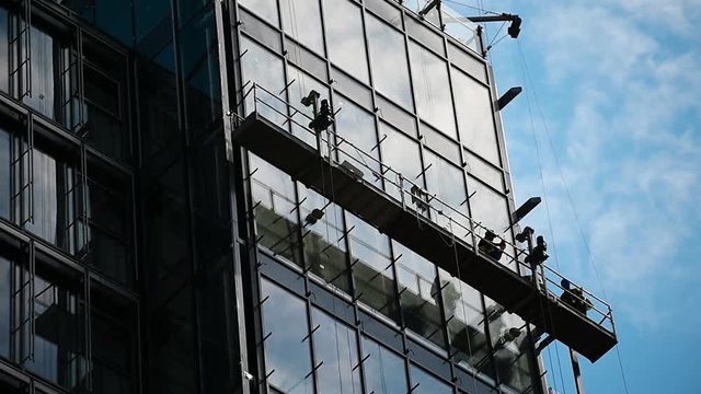 Construction workers on a suspended platform on a skyscraper glass facade