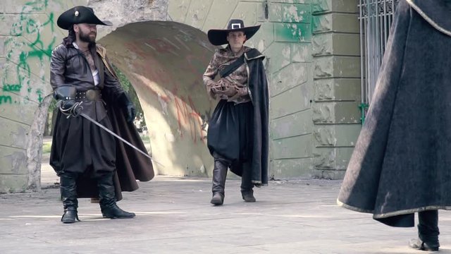 The musketeer gives the sword to the ally and they fight against the man in black clothes, slow motion