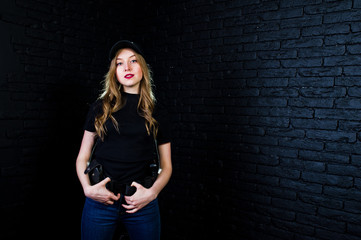 FBI female agent in cap and with gun at studio against dark brick wall.