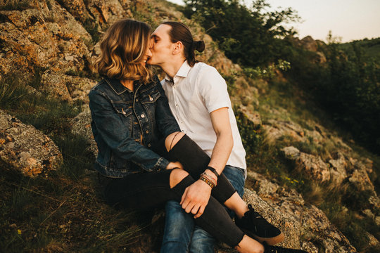 Young man kissing his girlfriend while sitting on rocky mountain