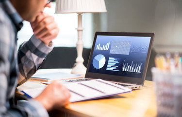 Man reading business report paper. Laptop with financial graphs, statistics and market progress. Entrepreneur counting budget or income tax. Businessman working in home office.
