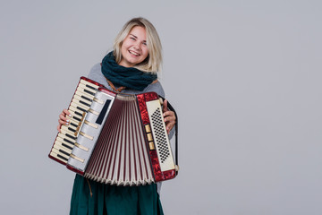 Pretty young happy woman with accordion. Playing music. Studio Shot. Over gray background