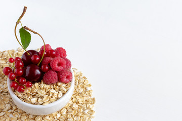 Oatmeal with cherries, raspberries and red currants in a cup against a white background.