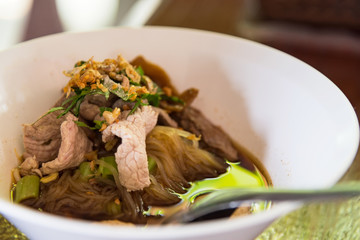 Asian pork noodle soup with beef meatball, pork and with fresh vegetable on dark wood table, street food, hot and spicy noodle soup, asian food. Close up noodles.Bangkok,Thailand.
